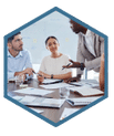 A group of employees gathered around a table with laptops, tablets, and notebooks, learning how to create project plans, schedules, and budgets. The facilitator stands next to a whiteboard filled with project management templates and tools.