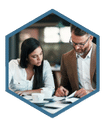 A group of employees sitting around a conference table looking over project plans and timelines during an on-site project management training session. The facilitator stands near a whiteboard with project management process diagrams.